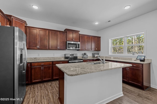 kitchen featuring appliances with stainless steel finishes, sink, dark hardwood / wood-style flooring, a kitchen island with sink, and light stone countertops