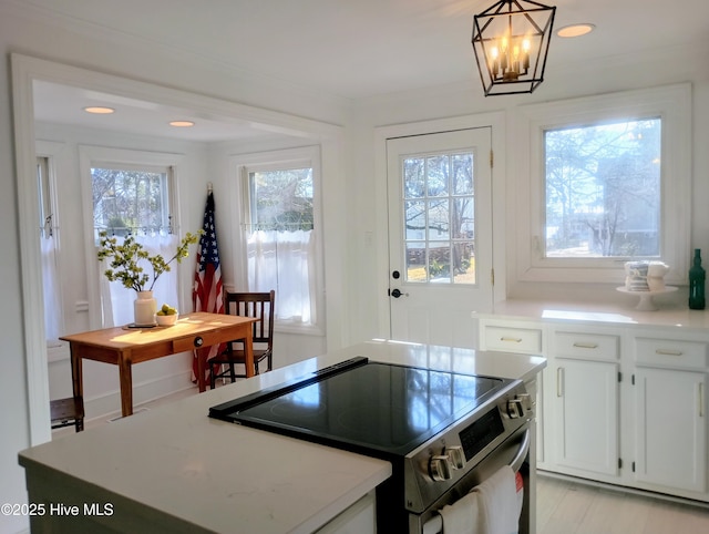 kitchen featuring a kitchen island, white cabinets, hanging light fixtures, crown molding, and stainless steel electric range