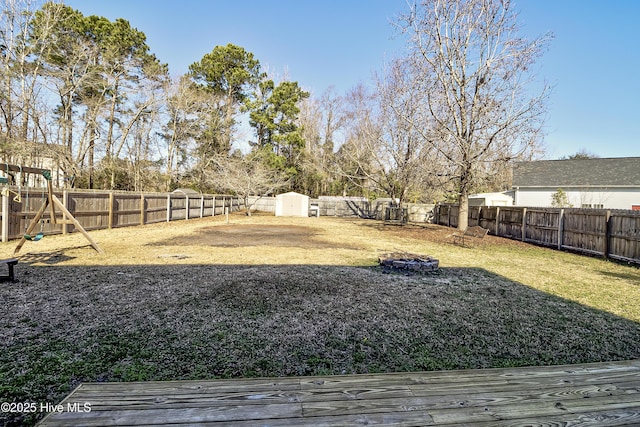 view of yard featuring a storage shed, a playground, a wooden deck, and an outdoor fire pit