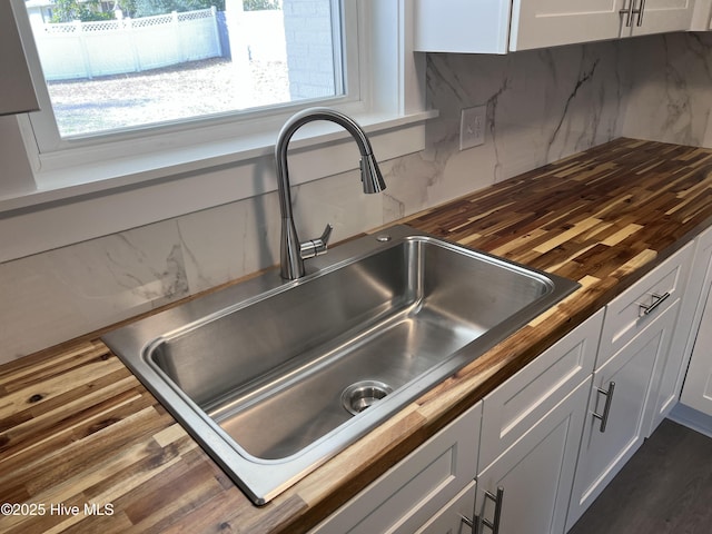 kitchen with white cabinetry, butcher block countertops, tasteful backsplash, and sink