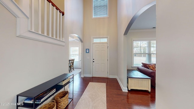 foyer entrance with dark wood-type flooring, crown molding, and a high ceiling