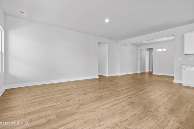 unfurnished living room with baseboards, visible vents, a notable chandelier, and light wood finished floors