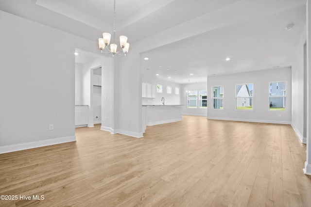 unfurnished living room with recessed lighting, a raised ceiling, light wood-style flooring, a chandelier, and baseboards