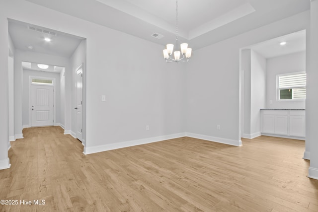 unfurnished dining area with light wood-style flooring, visible vents, a raised ceiling, and baseboards