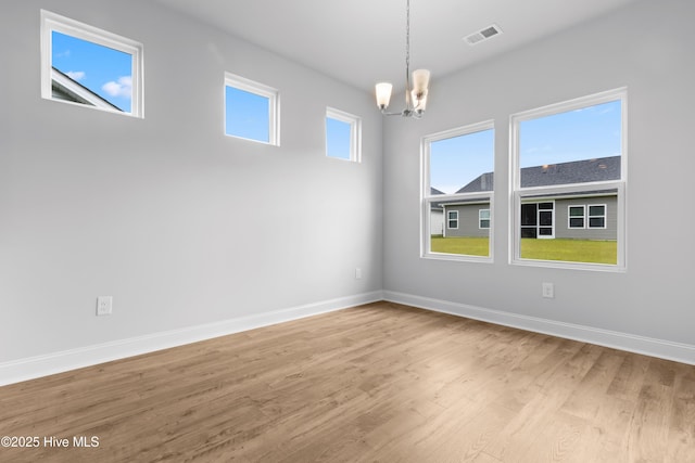 spare room with baseboards, visible vents, a chandelier, and wood finished floors