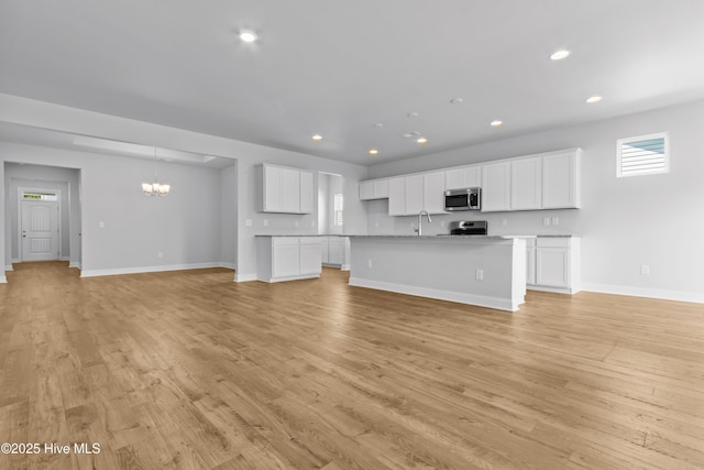 unfurnished living room with light wood-style floors, recessed lighting, baseboards, and an inviting chandelier