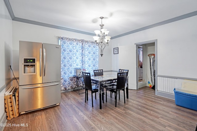 dining space with hardwood / wood-style flooring, crown molding, and an inviting chandelier