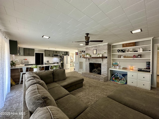 living room with built in shelves, sink, a brick fireplace, ceiling fan, and carpet