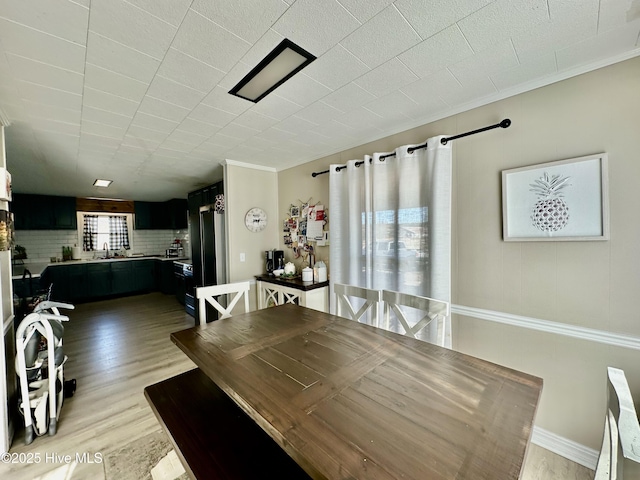 dining space with ornamental molding, sink, and light wood-type flooring