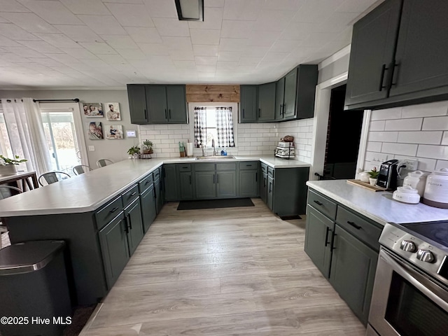 kitchen featuring stainless steel electric stove, sink, decorative backsplash, kitchen peninsula, and light hardwood / wood-style flooring