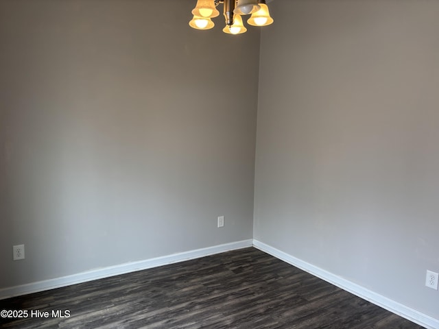 spare room featuring dark wood-type flooring and a chandelier