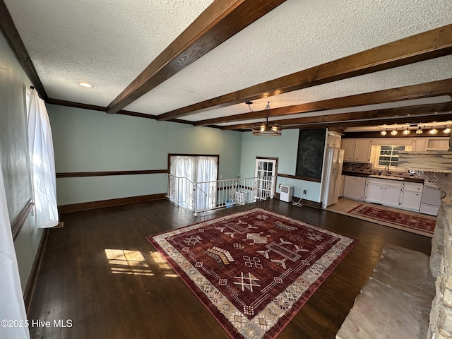 unfurnished living room with a textured ceiling, a sink, baseboards, beam ceiling, and dark wood finished floors