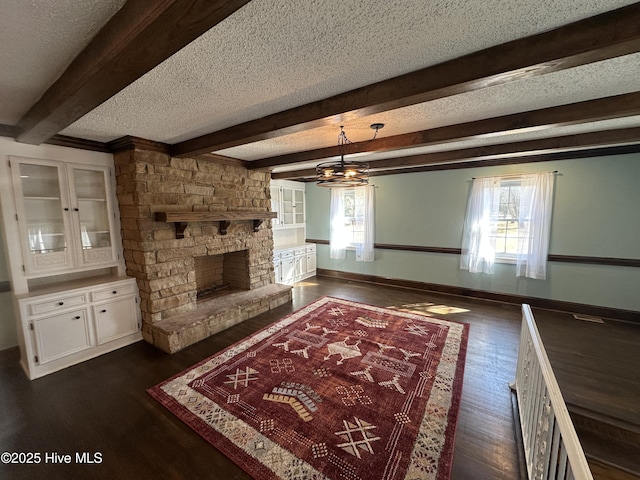 unfurnished living room featuring baseboards, dark wood-style floors, beamed ceiling, a textured ceiling, and a stone fireplace