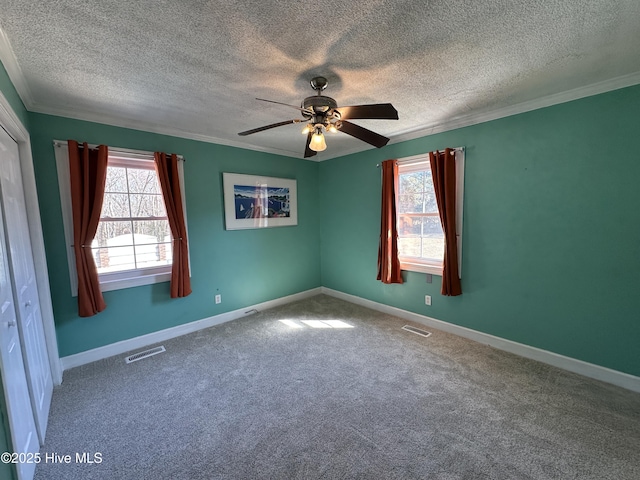 carpeted empty room with a ceiling fan, visible vents, and crown molding