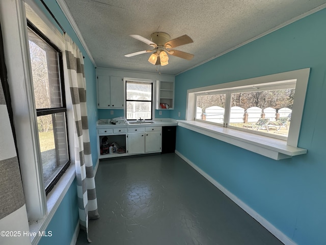 kitchen featuring baseboards, crown molding, a textured ceiling, concrete floors, and a sink