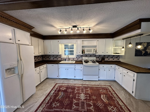 kitchen featuring dark countertops, hanging light fixtures, white cabinets, a sink, and white appliances