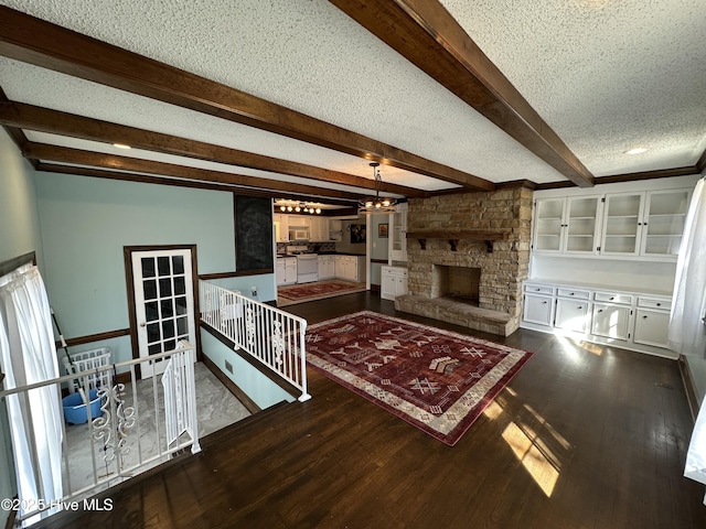 unfurnished living room with beam ceiling, dark wood finished floors, a textured ceiling, and a stone fireplace