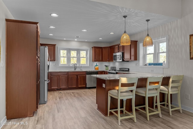 kitchen with hanging light fixtures, stainless steel appliances, light hardwood / wood-style floors, a kitchen bar, and kitchen peninsula