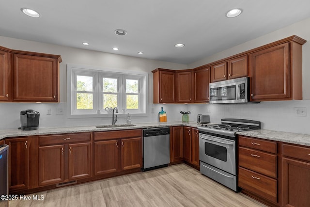 kitchen featuring appliances with stainless steel finishes, sink, backsplash, light stone counters, and light wood-type flooring