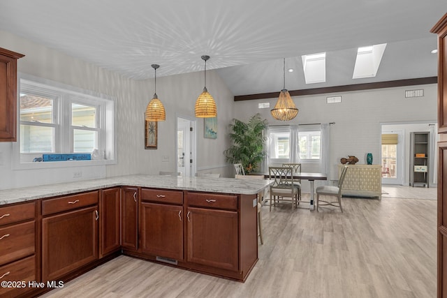 kitchen with vaulted ceiling with skylight, decorative light fixtures, kitchen peninsula, light stone countertops, and light hardwood / wood-style flooring