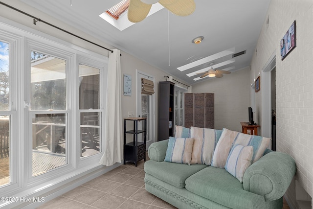 living room with light tile patterned flooring, ceiling fan, brick wall, and lofted ceiling with skylight