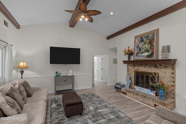 living room with ceiling fan, vaulted ceiling with beams, a fireplace, and light hardwood / wood-style flooring