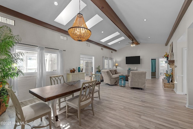 dining area with a skylight, high vaulted ceiling, light wood-type flooring, beam ceiling, and ceiling fan with notable chandelier