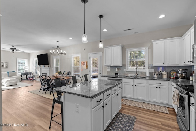 kitchen featuring white cabinetry, stainless steel electric range oven, a center island, hanging light fixtures, and a kitchen breakfast bar