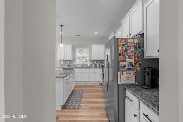 kitchen with stainless steel fridge, decorative light fixtures, white cabinets, and light hardwood / wood-style flooring