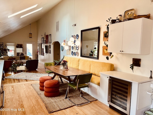 dining room featuring wine cooler, a skylight, high vaulted ceiling, and light wood-type flooring