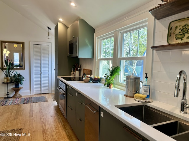 kitchen featuring sink, vaulted ceiling, appliances with stainless steel finishes, light hardwood / wood-style floors, and backsplash