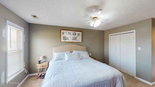 carpeted bedroom with a textured ceiling, ceiling fan, and a closet