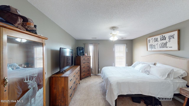 bedroom with ceiling fan, light colored carpet, and a textured ceiling