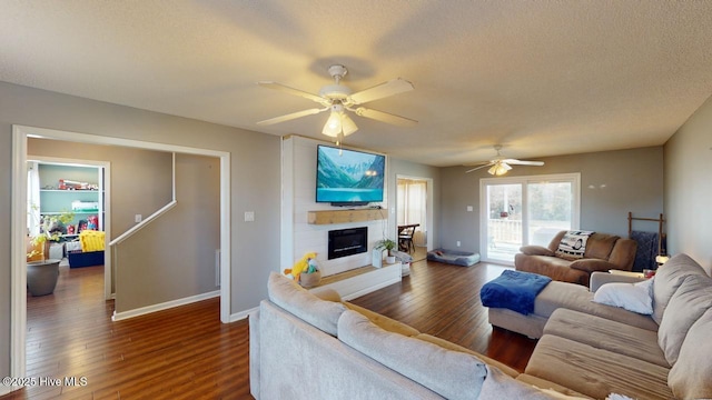 living room featuring ceiling fan, dark wood-type flooring, a large fireplace, and a textured ceiling