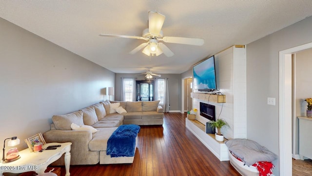 living room featuring ceiling fan, a large fireplace, dark hardwood / wood-style flooring, and a textured ceiling