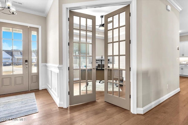 doorway to outside featuring ornamental molding, wood-type flooring, ceiling fan with notable chandelier, and french doors