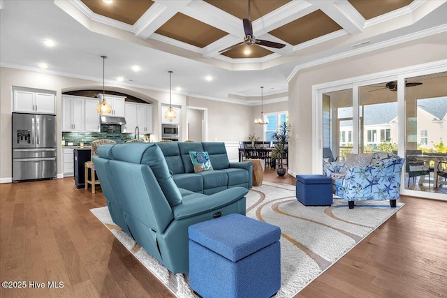 living room with ceiling fan, dark hardwood / wood-style floors, coffered ceiling, ornamental molding, and beamed ceiling