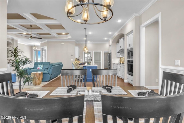 dining area featuring coffered ceiling, sink, an inviting chandelier, crown molding, and light hardwood / wood-style floors