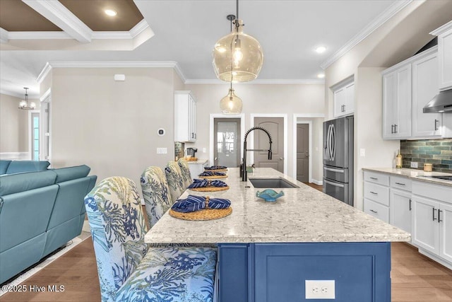 kitchen with pendant lighting, sink, stainless steel fridge, light stone countertops, and a center island with sink