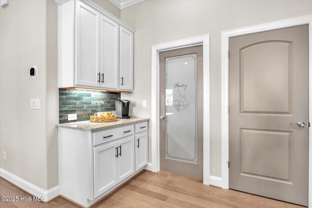 kitchen with light stone countertops, decorative backsplash, light hardwood / wood-style floors, and white cabinets