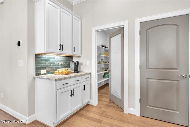 bar with tasteful backsplash, white cabinetry, light stone counters, and light hardwood / wood-style flooring