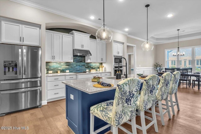 kitchen featuring appliances with stainless steel finishes, a center island with sink, white cabinets, and a kitchen bar