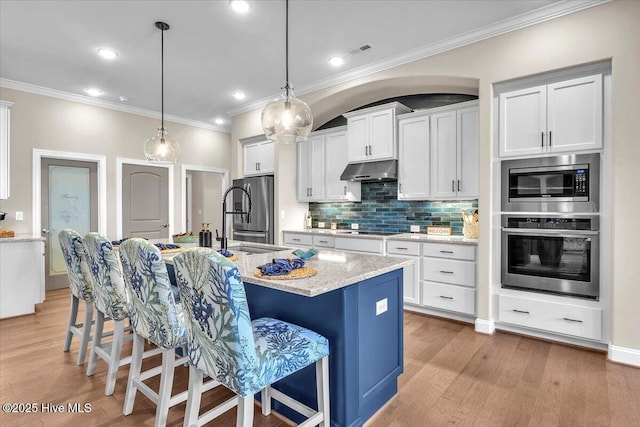 kitchen featuring a breakfast bar, white cabinetry, hanging light fixtures, appliances with stainless steel finishes, and a kitchen island with sink