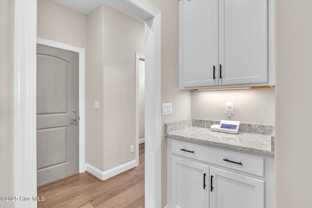 bar featuring white cabinetry, light stone counters, and light hardwood / wood-style flooring