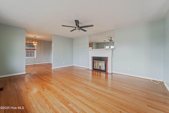 unfurnished living room featuring light hardwood / wood-style flooring, ceiling fan with notable chandelier, a fireplace, and plenty of natural light