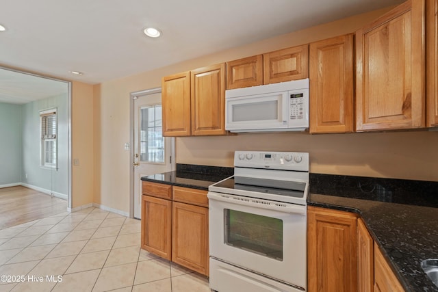 kitchen with white appliances, dark stone counters, and light tile patterned flooring