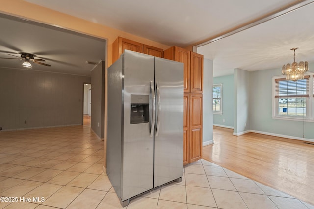 kitchen with stainless steel refrigerator with ice dispenser, decorative light fixtures, light tile patterned floors, wooden walls, and ceiling fan with notable chandelier