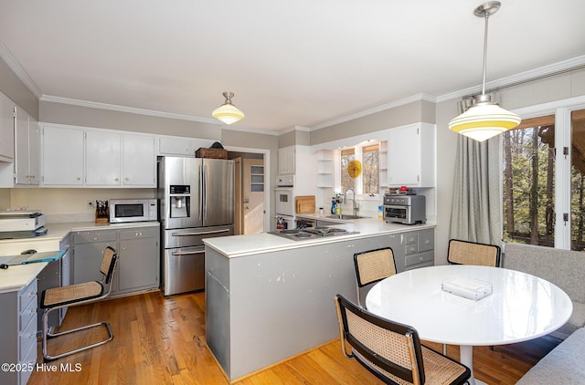 kitchen featuring sink, hanging light fixtures, light hardwood / wood-style floors, stainless steel appliances, and crown molding