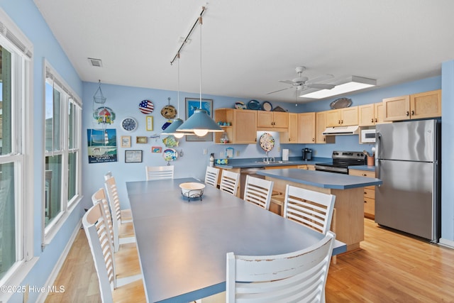 kitchen with light brown cabinetry, hanging light fixtures, ceiling fan, stainless steel appliances, and light wood-type flooring