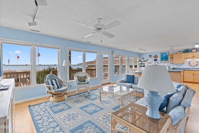 living room featuring ceiling fan, sink, a textured ceiling, and light hardwood / wood-style flooring